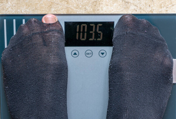 Человек, взвешивающий себя по электронной шкале в черных носках. Концепция питания
