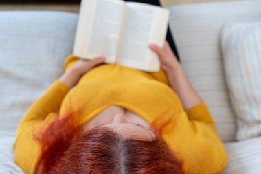 Sarı kazaklı güzel kızıl kadın oturma odasında rahatlamış bir kitap okuyor. Eğlence konsepti