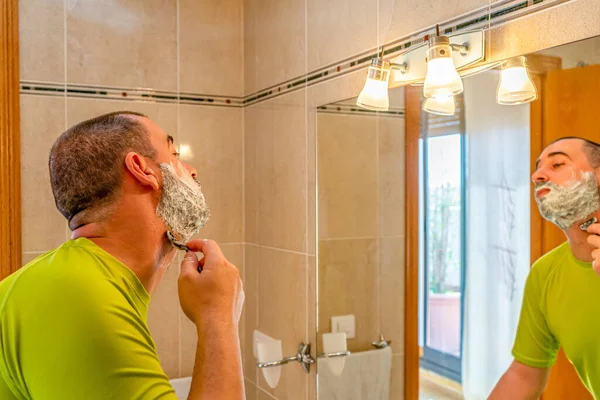 身穿开心果绿衬衫 在镜子前刮胡子的男人 — 图库照片
