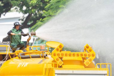 Bangkok, Tayland - 28 Eylül 2019: Şehir parkında ağaçlarını sulayan bir işçi sarı kamyondaki bir tankın yüksek basınçlı pompasını kullanıyor.