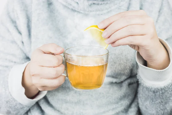 Tea mug in female hands. Woman drinking hot tea with lemon. Close up.