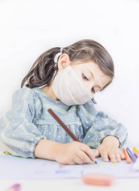 Evde ya da okulda maskeyle resim çizen küçük bir kız. Coronavirus. Covid 19