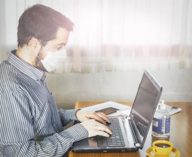 Maske ve el dezenfektanı ile evde çalışan bir adam. Coronavirus. Covid 19
