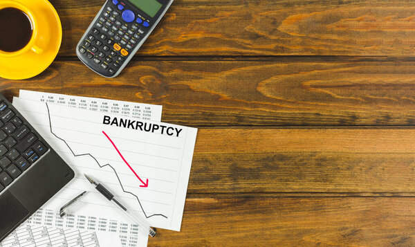 Bankruptcy chart with laptop and calculator on a brown wooden table. Space for text.