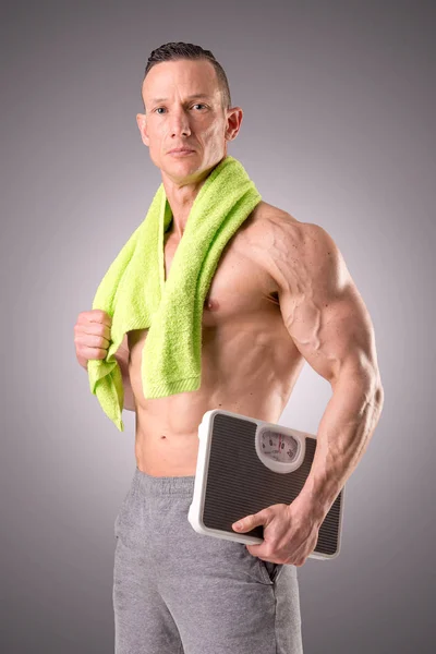Muscular man holding scales — Stock Photo, Image