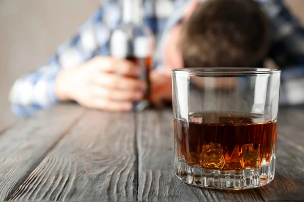 Μεθυσμένος άνθρωπος κρατά μπουκάλι στο ξύλινο τραπέζι με ένα ποτήρι ουίσκι, co — Φωτογραφία Αρχείου