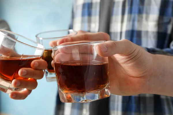 Manos masculinas sostiene vasos con whisky sobre fondo azul. Salud. — Foto de Stock