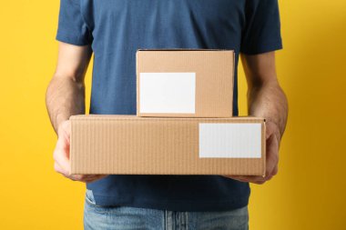 Delivery man hold blank boxes against yellow background, space f