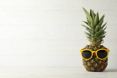 Beyaz ahşap arka planda güneş gözlüklü ananas. 