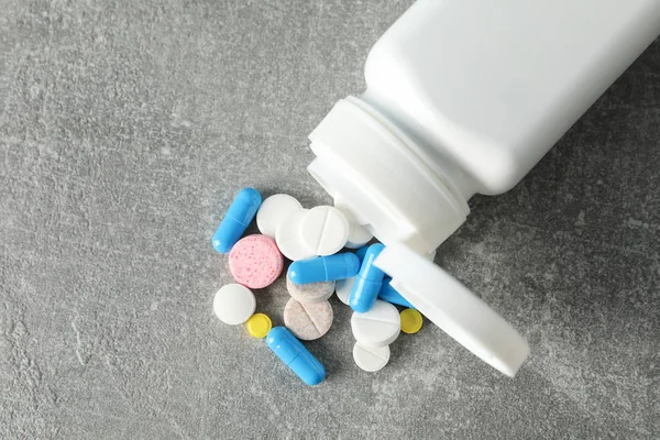 Medical container and pills on grey background, close up