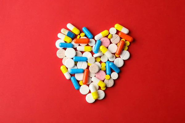 Herz aus Pillen auf rotem Hintergrund, Platz für Text. Ansicht von oben — Stockfoto