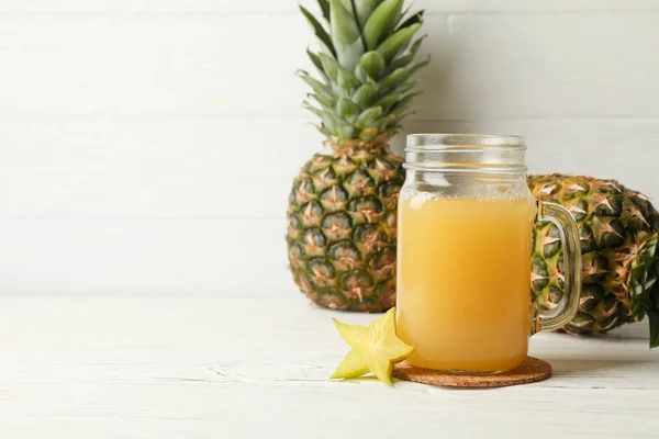 Glass jar with juice and pineapples on white wooden background, — Stock Photo, Image