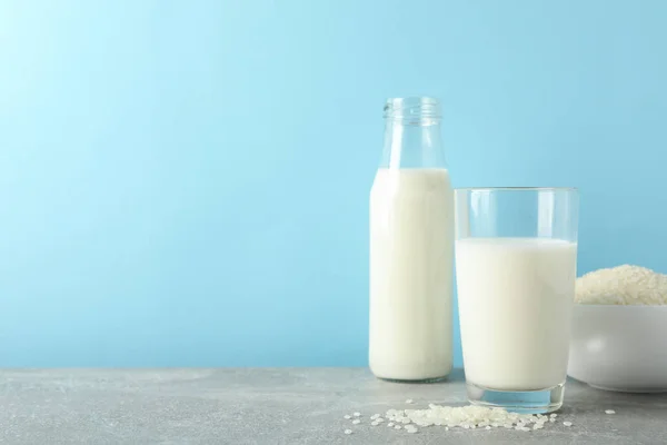 Bottiglia di latte di riso, bicchiere di latte di riso, piatto di riso su tavola grigia — Foto Stock