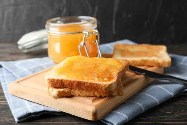 Toast met abrikozenjam, bord, handdoek en kruik op houten achterzijde — Stockfoto