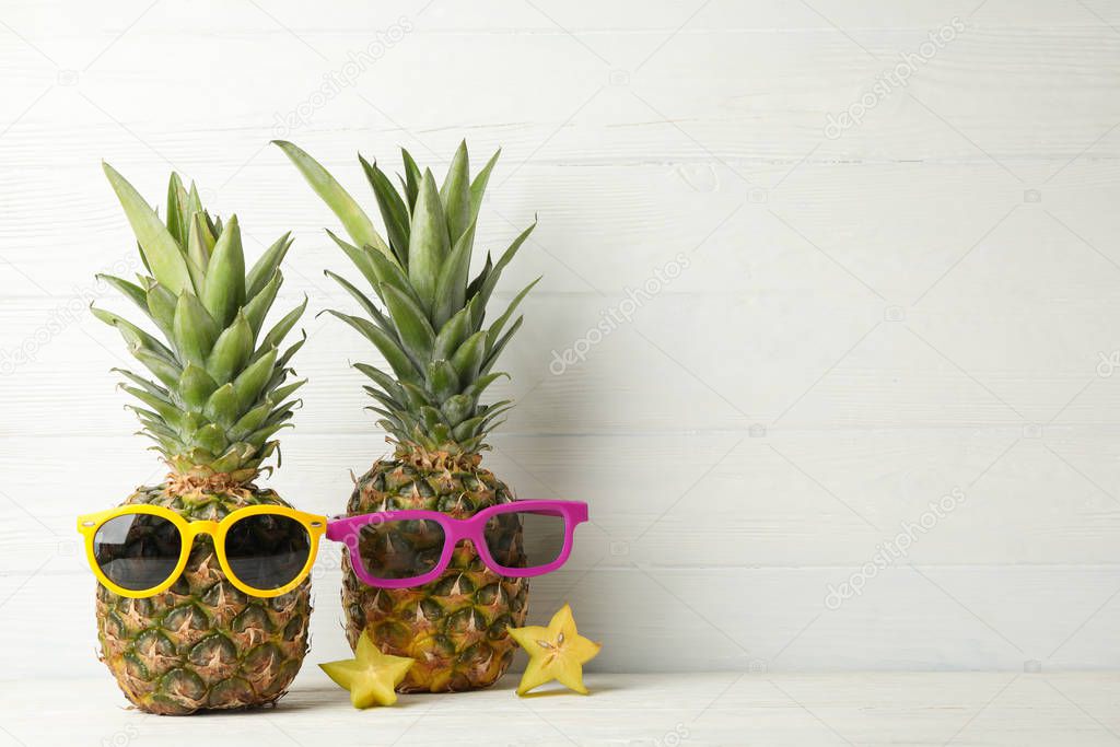 Pineapples with sunglasses on white wooden background, space for