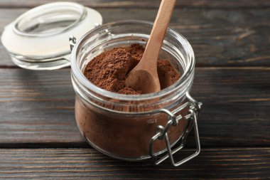 Cam kavanoz, kakao tozu ve ahşap arka planda kaşık.