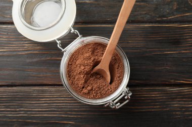 Cam kavanoz, kakao tozu ve ahşap arka planda kaşık.