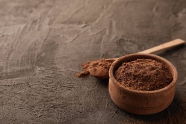 Kahverengi arka planda kakao tozu ve kaşık olan kâse, yakın plan.