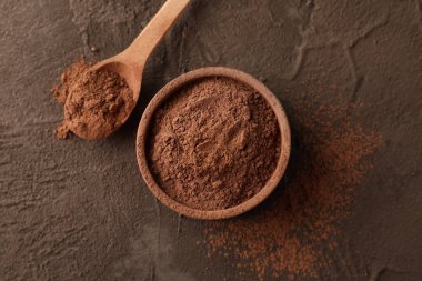 Kahverengi arka planda kakao tozu ve kaşık olan kâse, yakın plan.