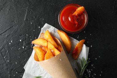 Pakette fırında patates, siyah arkaplanda kırmızı sos.