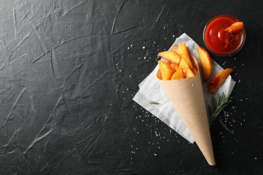 Pakette fırında patates, siyah arkaplanda kırmızı sos.