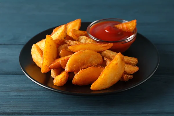 Plate with slices of baked potato wedges, red sauce on blue wood — Stock Photo, Image