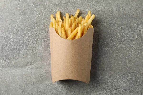 Шматочки гарячої картоплі фрі в коробці на сірому фоні, простір для — стокове фото