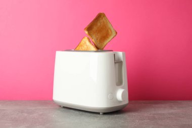 Tost makinesi ve ekmek dilimleri gri masada pembe arka planda, 