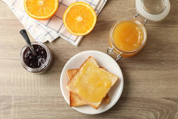 Toasts sur assiette, confiture, serviette et orange sur fond bois, dessus — Photo