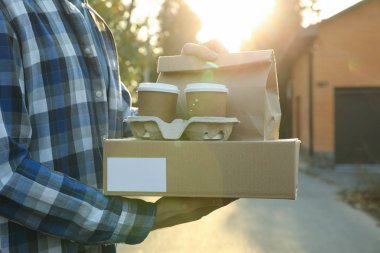 Adamın elinde boş kutu, kahve fincanı ve kağıt paket var. Hazır.