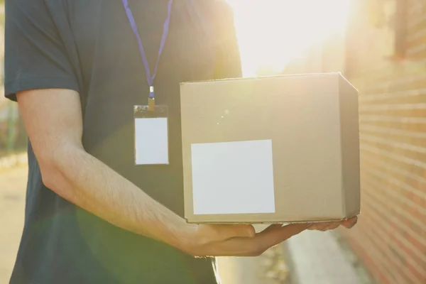Чоловік-доставка з значком тримає порожню коробку на відкритому повітрі, місце для тексту — стокове фото