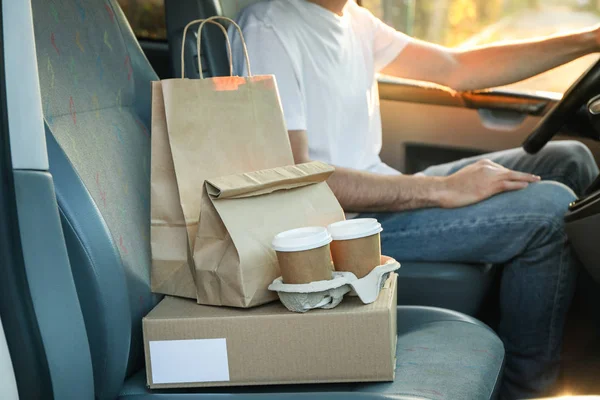Blank box, coffee cups, paper packages and courier in car. Deliv — Stock Photo, Image