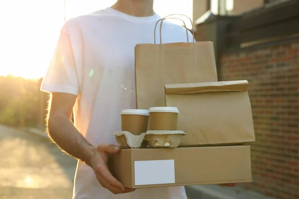Чоловік тримає чисту коробку, чашки для кави та паперовий пакет на відкритому повітрі. Делі — стокове фото