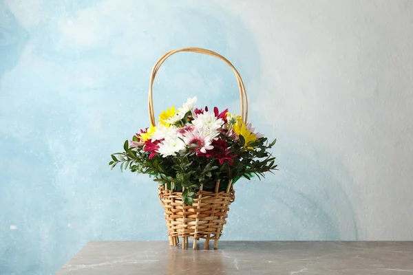 Mavi arka planda gri masadaki çiçekli hasır sepet — Stok fotoğraf