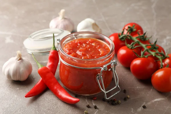 Chili sauce in glass jar and ingredients on grey background, clo — Stock Photo, Image