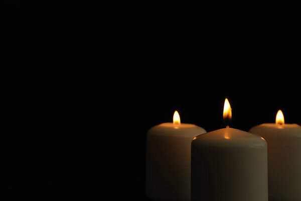 Glowing candles on black background, space for text