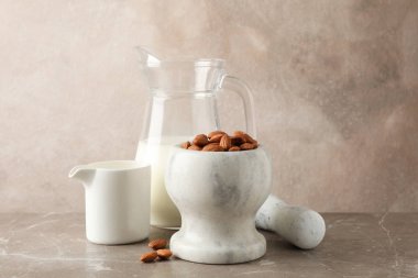 Bir sürahi badem sütü, kahverengi zemin üzerinde badem tohumları olan havan topu.