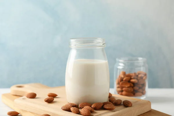 Glass of almond milk, almond seeds on white table again blue bac — Stock Photo, Image