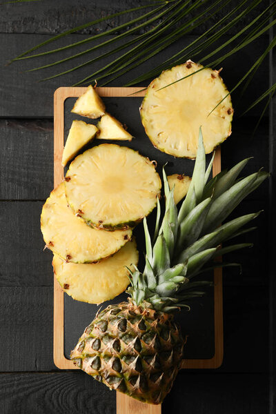 Cutting board with pineapple and palm branch on wooden backgroun