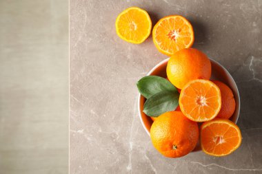 Mandalinalar ve yapraklar kasede, gri masada, üst tarafta.