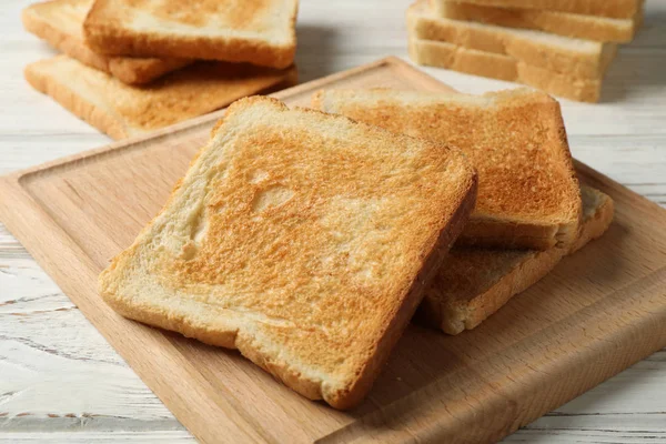 Brett mit Toasts auf weißem Holzgrund, Nahaufnahme — Stockfoto