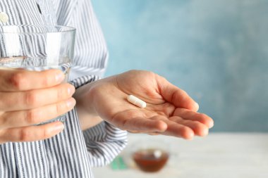 Kadın mavi arka planda hap ve bir bardak su tutuyor.