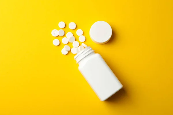 Frasco médico en blanco y pastillas sobre fondo amarillo, vista superior — Foto de Stock