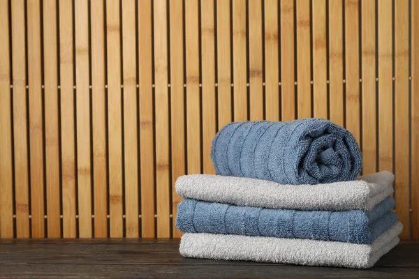 Folded towels on wooden table against bamboo background, space f — Stock Photo, Image