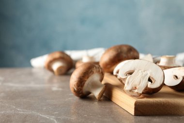 Taze şampiyon mantarlar ve gri arka planda ahşap tahta.