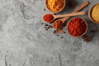 Gri arka planda farklı baharatlarla kaşıklar ve kaseler, en üstteki v