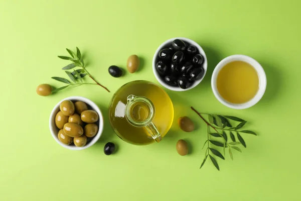 Aceitunas, botella y tazón con aceite de oliva sobre fondo verde, tapa — Foto de Stock