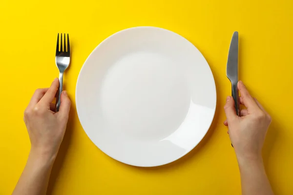 Female hands hold fork and knife on yellow background with plate — 스톡 사진