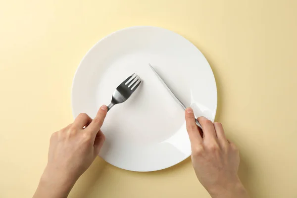 Female hands hold fork and knife on beige background with plate, — 스톡 사진