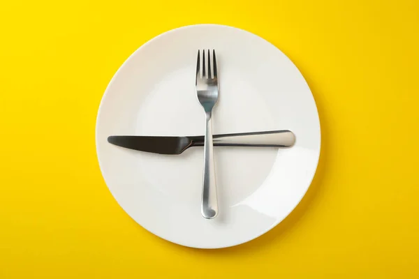 Plate with fork and knife on yellow background, top view — 스톡 사진